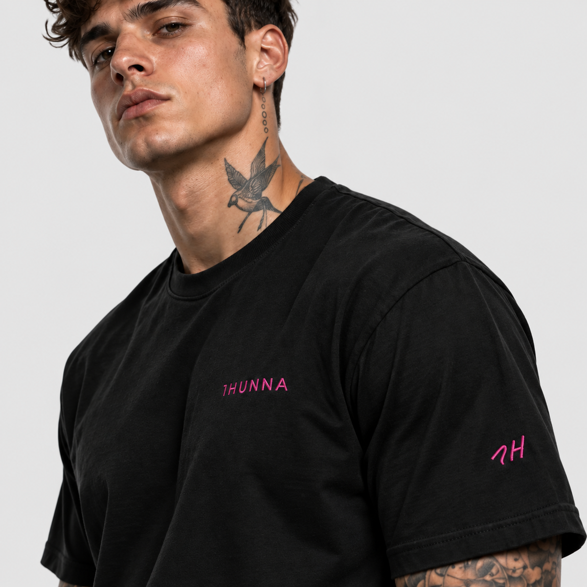 Close-up of pink 1HUNNA chest and sleeve details on the black Casual T-shirt